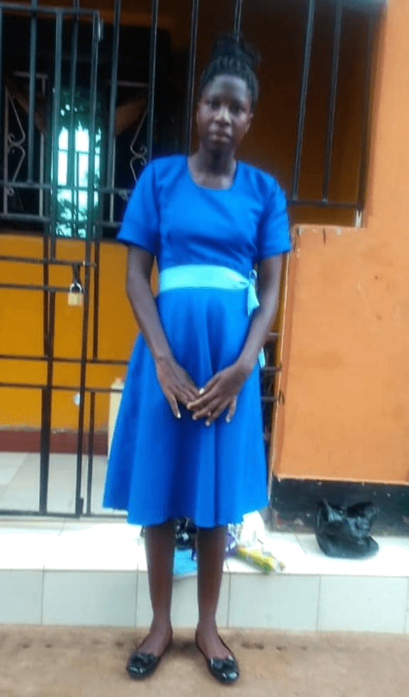 A woman in blue dress standing next to a fence.